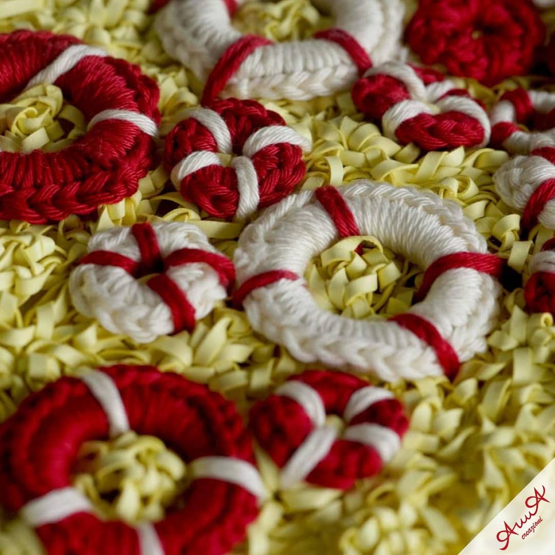 Miniature red and white crocheted lifebuoys resting on a bed of yellow shredded paper.