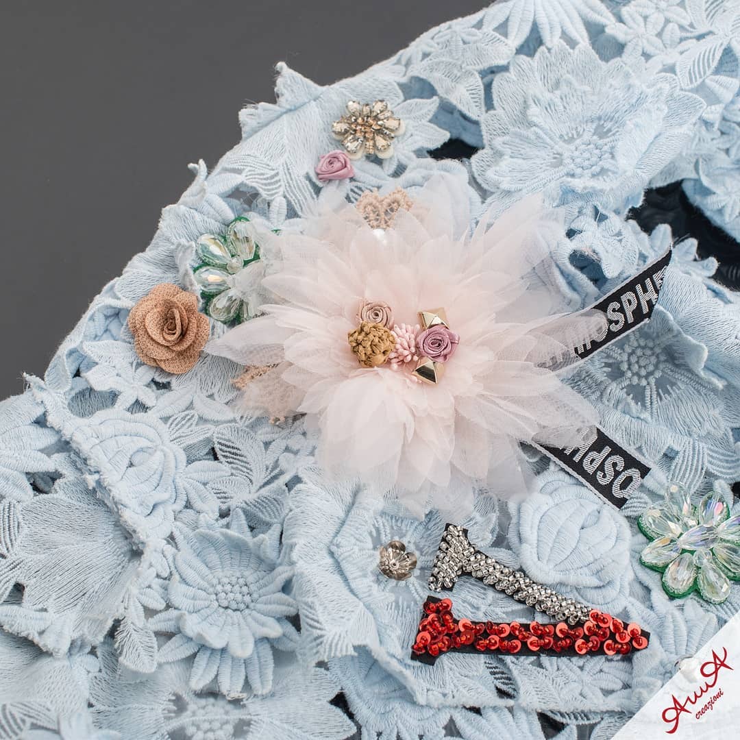 Light blue lace fabric featuring a large pink flower, beaded jewels, and red sequined accents.