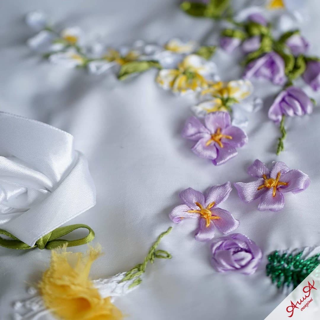 Delicate purple and yellow satin ribbon flowers embroidered on white fabric with green stems.