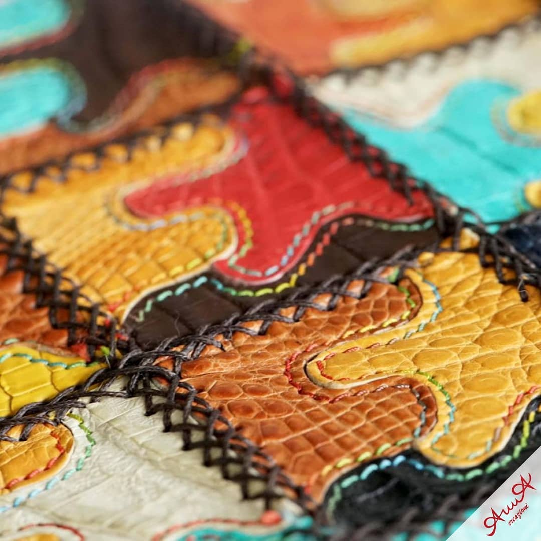 Close-up of colorful, textured leather patches with wavy edges joined by thick braided stitching.