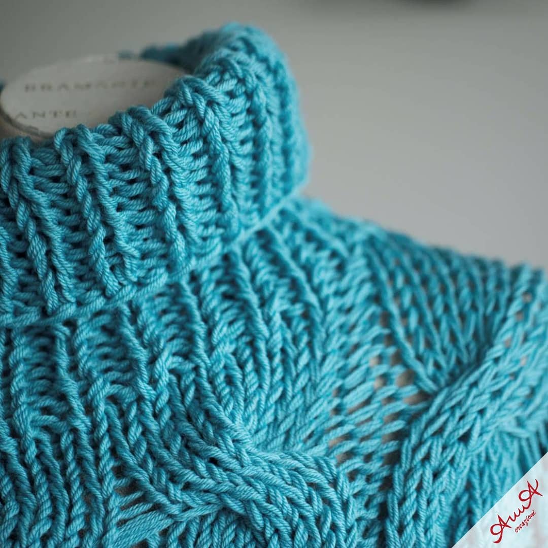 Turquoise blue knitted sweater featuring a thick ribbed turtleneck and intricate, textured cable stitch patterns.