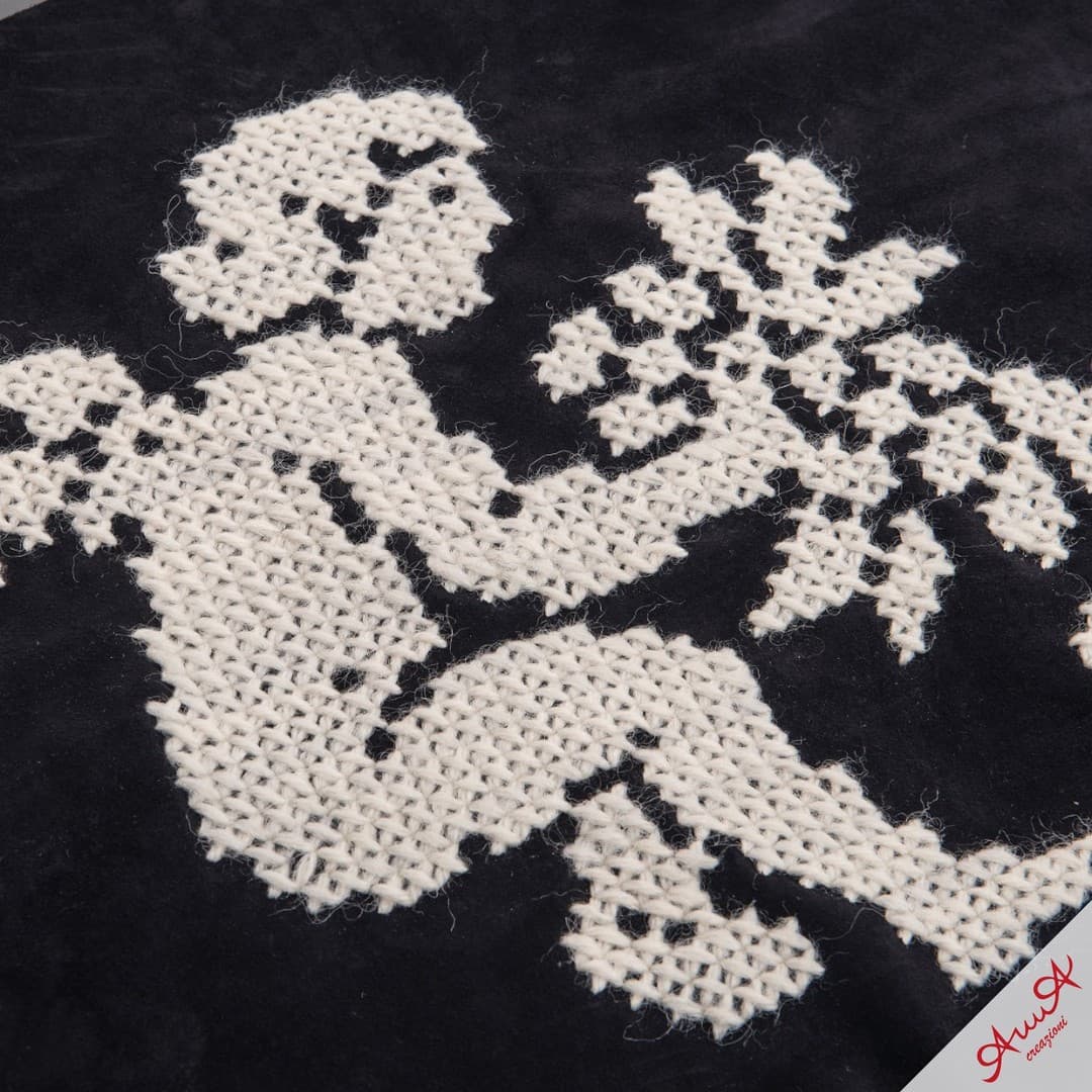 Intricate white cross-stitch embroidery of a stylized mythical creature on a black fabric background.