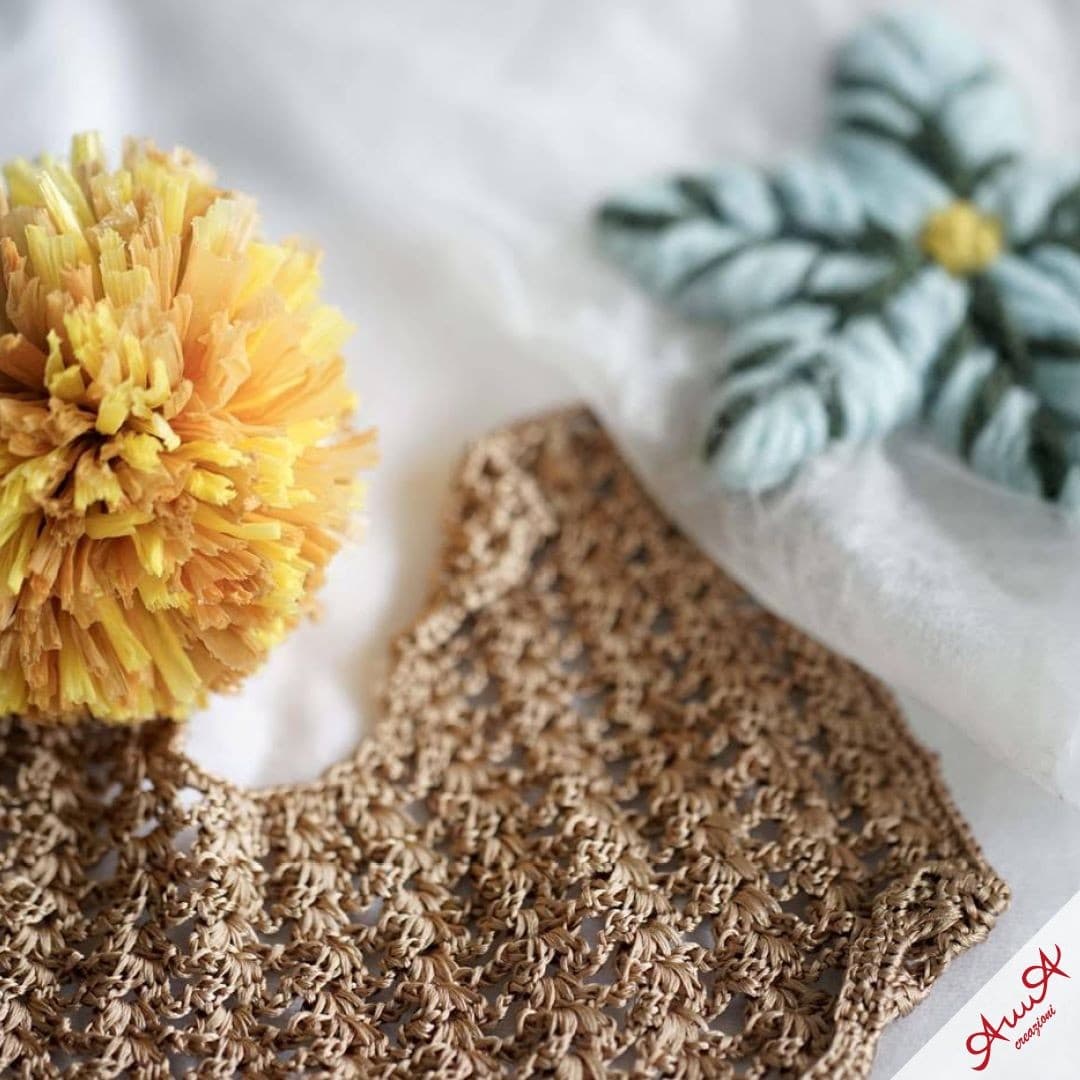 Brown crocheted lace fabric next to a yellow raffia pom-pom on a white background.