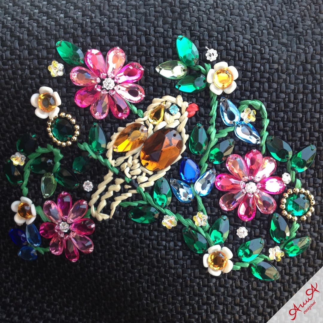 Colorful jewel-encrusted bird and flowers embroidered onto a black woven fabric background.