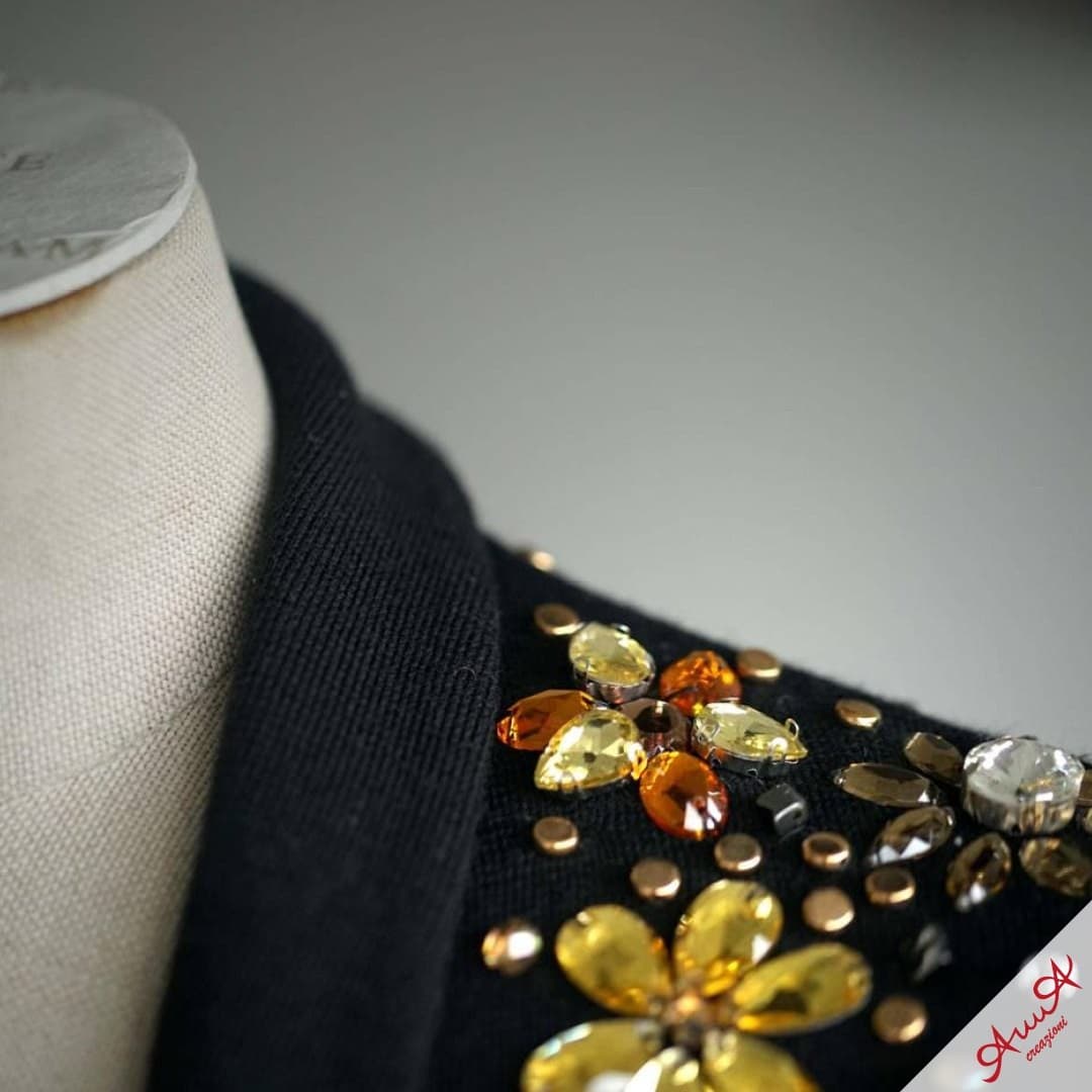 Close-up of black jacket shoulder embellished with yellow and amber crystal flowers and gold studs.